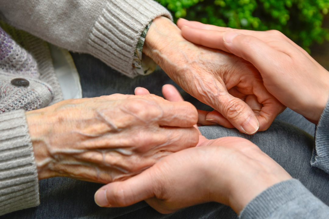 A caregiver offering support to an elderly individual, symbolizing the compassionate care provided to someone living with dementia.
