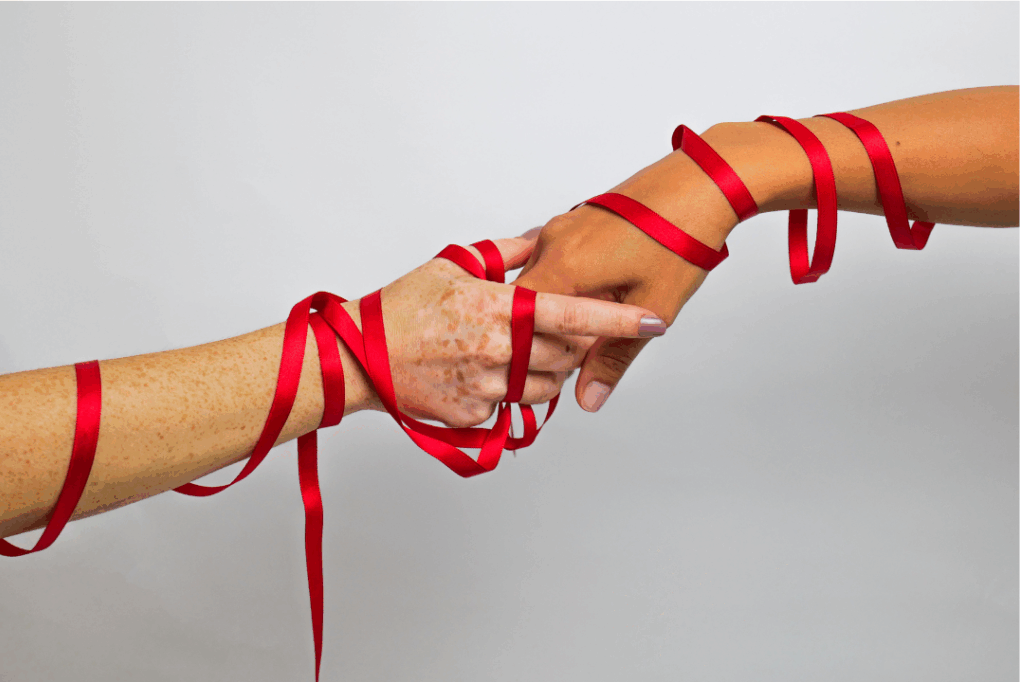 Two hands of different skin tones wrapped together with a red ribbon, symbolizing connection, unity, or support.