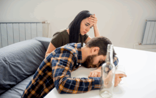 Worried woman comforting a distressed man with alcohol in front of him, highlighting the emotional toll of supporting a partner struggling with substance use.