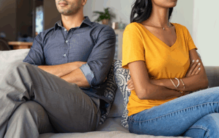 A couple sitting on a couch with arms crossed, facing away from each other, expressing emotional distance and conflict