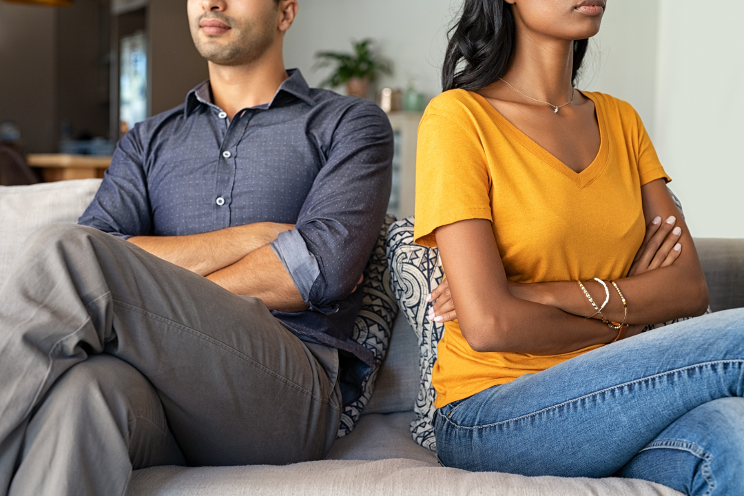 A couple sitting on a couch with arms crossed, facing away from each other, expressing emotional distance and conflict